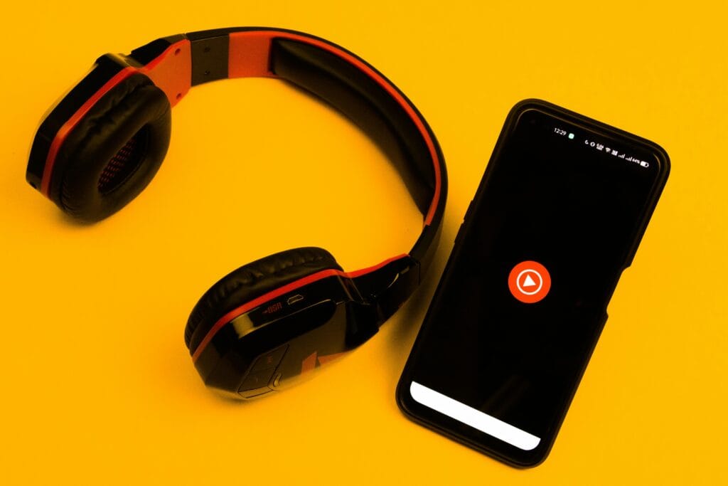 Wireless headphones and smartphone with play icon on a vibrant yellow background.